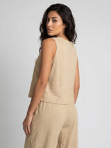 Back view of woman wearing a sand beige linen sleeveless crop top and wide-leg pants, over-the-shoulder glance, neutral studio background