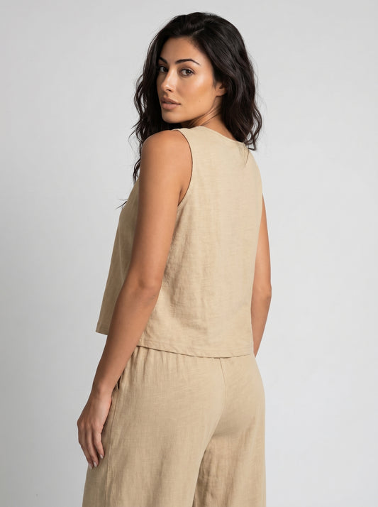 Back view of woman wearing a sand beige linen sleeveless crop top and wide-leg pants, over-the-shoulder glance, neutral studio background