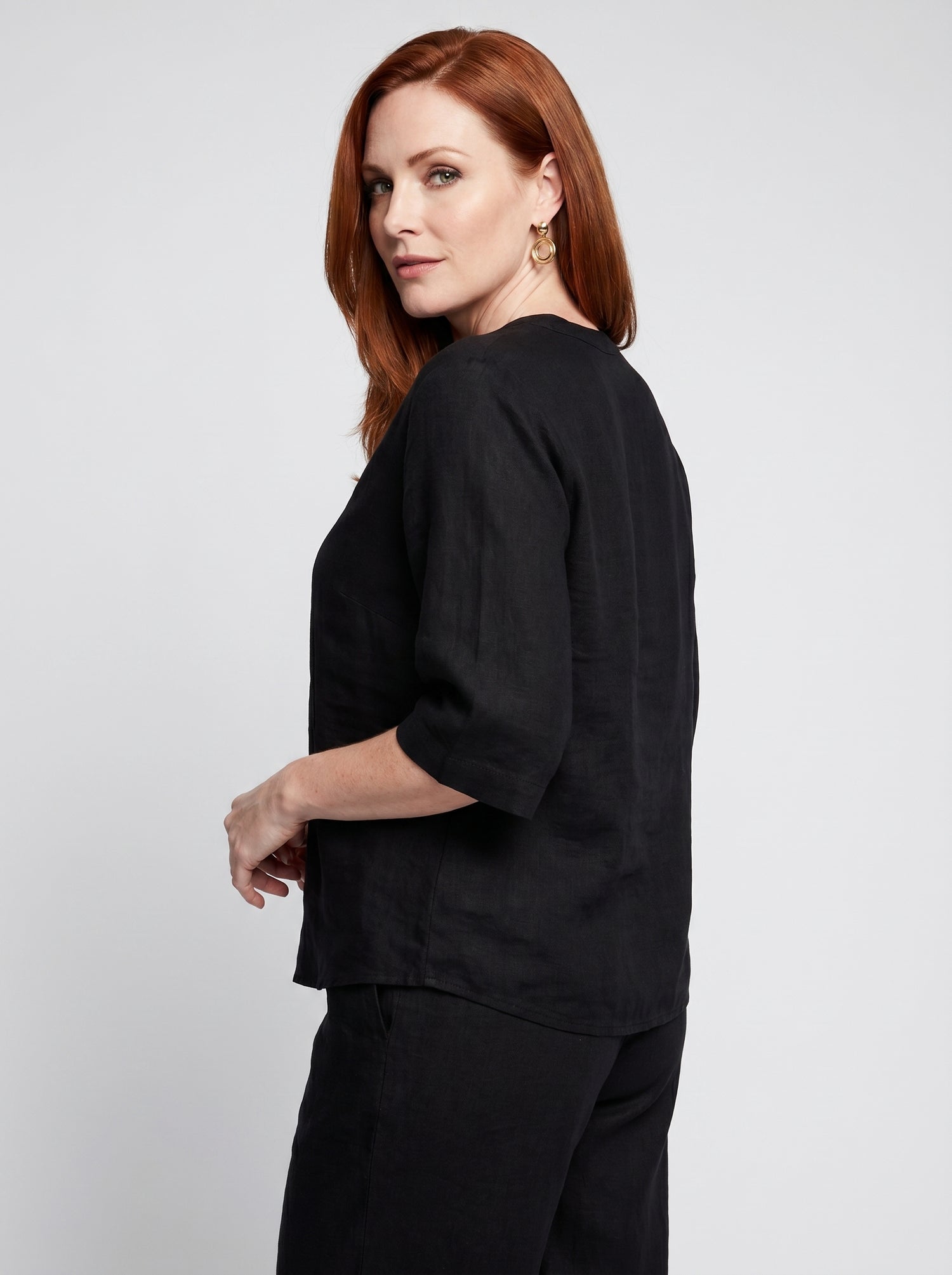 Side profile of woman wearing a black 100% polyester V-neck top with elbow-length sleeves and gold hoop earrings, paired with matching black shorts